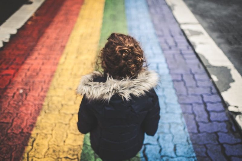 young woman from behing walking along a rainbow coloured path young woman from behing walking along a rainbow coloured path