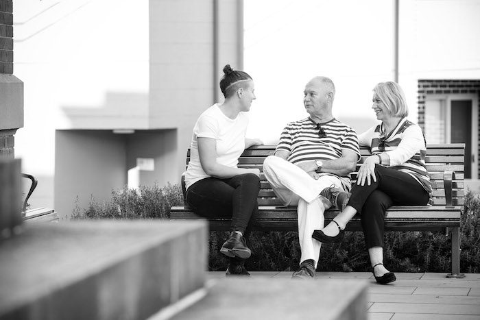 Black and white picture of 3 people sitting on a bench talking Black and white picture of 3 people sitting on a bench talking